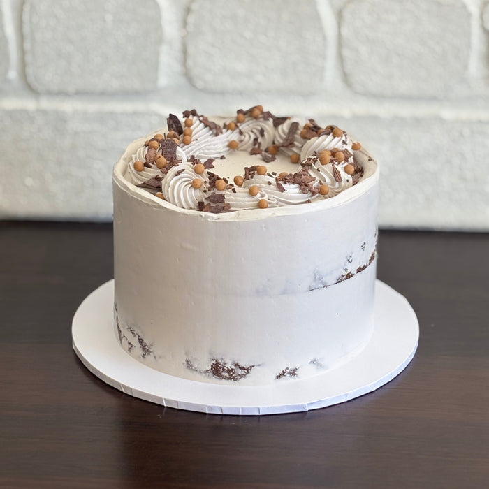chocolate mud cake with white chocolate ganache and salted caramel sauce. Decorated with swiss meringue semi naked finish, caramel crispearls and chocolate shavings