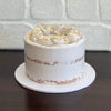 coconut mud cake layered with white chocolate ganache and finished with a swiss meringue semi naked buttercream. Decorated with white crispearls and toasted coconut