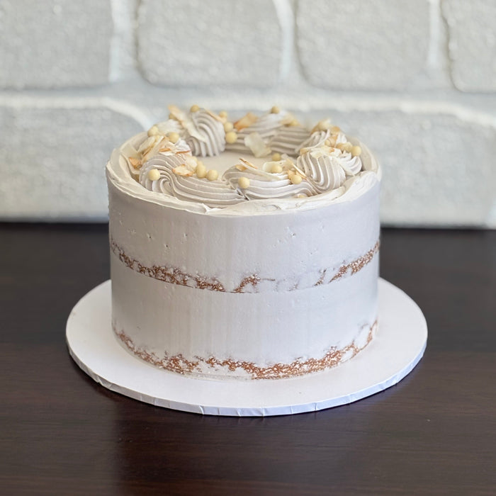 coconut mud cake layered with white chocolate ganache and finished with a swiss meringue semi naked buttercream. Decorated with white crispearls and toasted coconut
