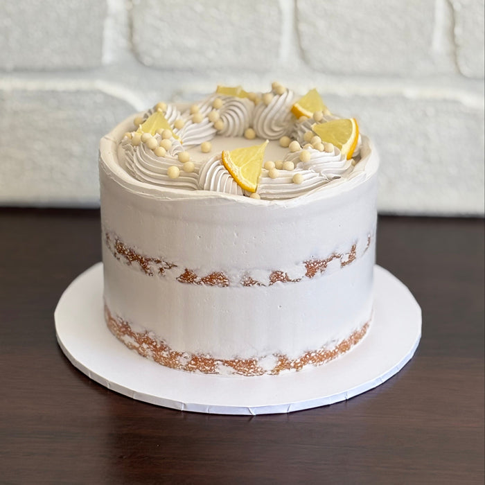 lemon mud cake layered with white chocolate ganache and lemon curd. Finished with a semi naked swiss meringue buttercream, white crisp pearls and fresh lemon pieces