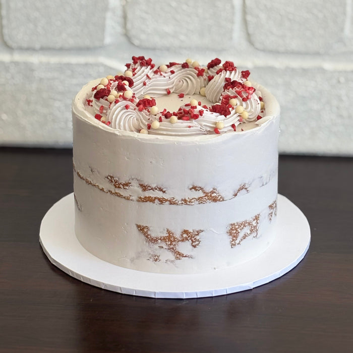 white mud cake layered with white chocolate ganache, raspberry and raspberry sauce. Finished with swiss mernigue semi naked buttercream, freeze dried raspberry and white crispearls